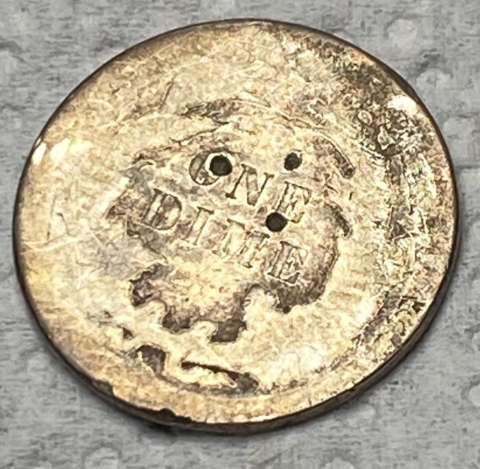 Worn dime with two holes, close-up view.